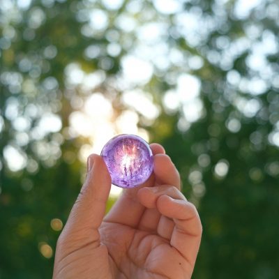 Amethyst quartz crystal ball in hand, natural green background.